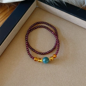 Macro detail of a garnet double-loop bracelet with amber beads on a beige jewelry tray