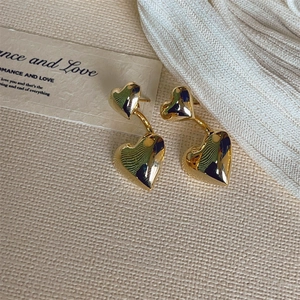 Macro shot of 18K gold double heart stud earrings with a high-polished mirror finish