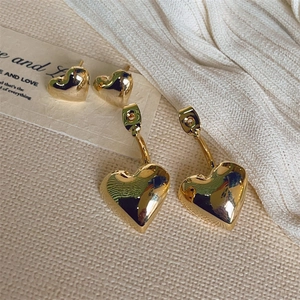 Golden heart-shaped stud and dangle earrings set displayed on a beige textured cloth