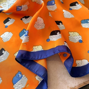 Dettaglio ravvicinato di un foulard in seta arancione con motivi di gatti e bordi blu