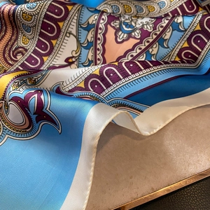 Detailed view of silk-like paisley scarf with rich blue and yellow patterns on gold tray