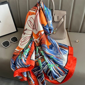 Elegant vintage print silk scarf in orange and royal blue draped on a luxury handbag