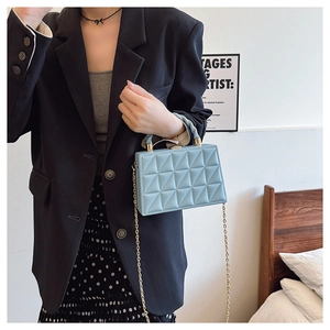 Detail of light blue geometric quilted mini box bag with gold chain and woven handle