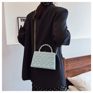 Detailed view of light blue quilted box bag with gold chain strap worn by a model