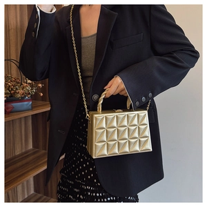 Detail of gold box handbag with geometric quilting and twisted top handle texture