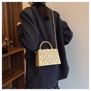 Detail of gold box clutch with geometric texture and twisted handle on a model