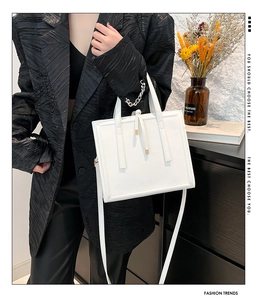 Detail view of structured white square handbag with adjustable strap and decorative stripes