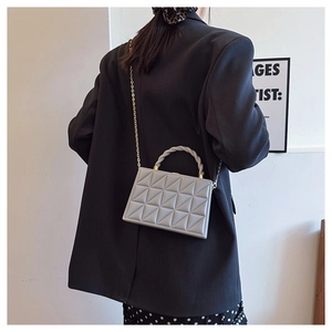 Detail of grey quilted box bag with woven ring handle and gold chain strap on model