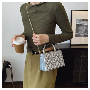 Detail of silver blue box bag with quilted pattern, gold chain, and metal handle