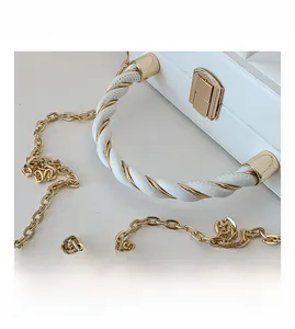 Detail of white quilted crossbody bag with gold chain and woven rope handle