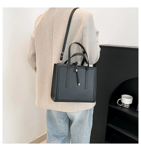 Rear view of a model carrying a structured black tote bag with vertical stitching