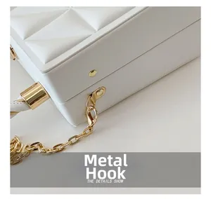 Detail of gold metal hook and chain connector on white embossed box handbag