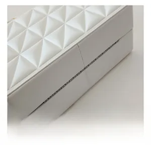 Detail of white quilted crossbody box bag featuring elegant diamond pattern and metal hinges