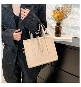 Chic beige tote bag with side fringe detail held by a model in a modern urban setting
