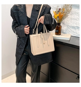 Beige rectangular tote bag featuring smooth leather texture and decorative tassel details