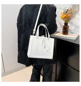 Close-up of a white leather crossbody bag with dual handles and elegant strap detailing