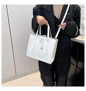 Close-up of white structured tote bag with tassels and gold hardware on a dark background