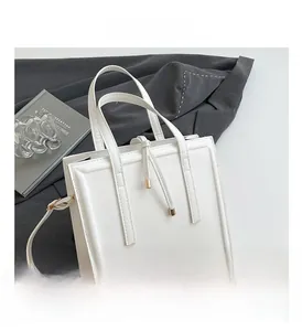 Detail of white minimalist square handbag with vertical stitching and golden hardware