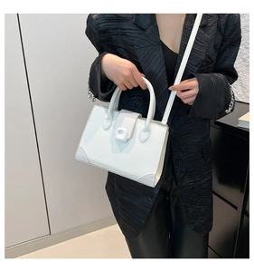 Close-up of white square handbag featuring grey crocodile pattern and metal lock detail