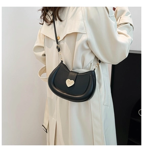 Détail du sac bandoulière noir en demi-lune avec boucle en forme de cœur doré sur un trench