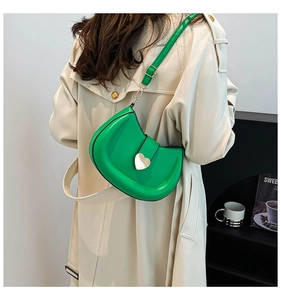 Détail du sac bandoulière demi-lune vert avec boucle cœur dorée sur un mannequin