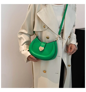 Détail du sac de selle vert vif avec fermoir cœur porté sur un trench-coat beige