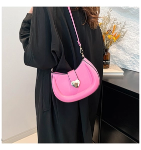 Détail d'un sac à bandoulière croissant rose vif avec boucle cœur dorée et texture en cuir