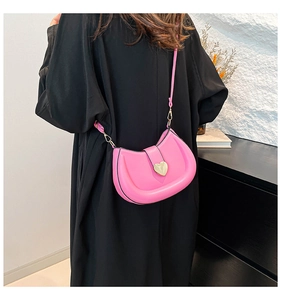 Détail du sac selle rose avec fermoir cœur porté sur un manteau noir contrastant