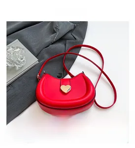 Détail d'un sac selle rouge avec boucle métallique en forme de cœur dorée et texture cuir