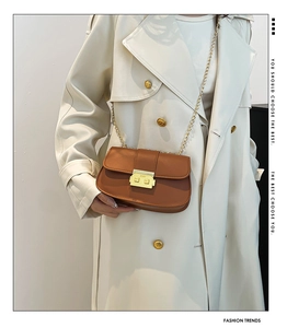 Sac bandoulière en cuir marron avec boucle dorée porté sur un trench-coat beige