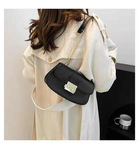 Détail d'un sac à bandoulière noir avec chaîne porté avec un manteau beige élégant