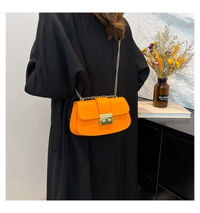 Détail d'un sac bandoulière orange vif avec chaîne dorée sur un manteau noir élégant