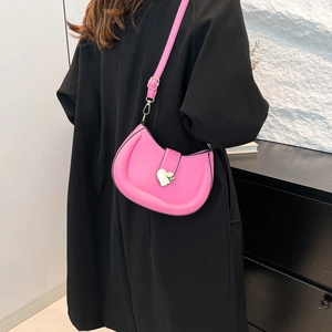 Sac demi-lune rose avec boucle en cœur en métal porté par un mannequin sur un manteau noir