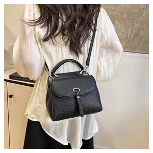 Detail of black lychee texture handbag worn crossbody with silver metal buckle and strap