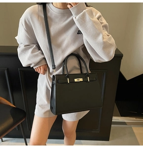 Detail of black structured handbag with gold turn-lock closure and leather top handle