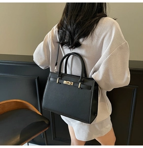 Model wearing a black cross-grain leather top-handle bag with gold hardware and strap
