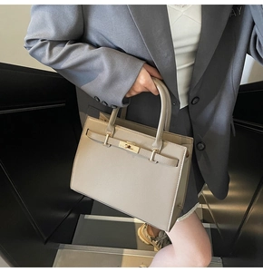 Detail of khaki leather handbag featuring metal twist lock and rounded top handles