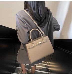 Detail view of khaki leather handbag with gold metal lock and shoulder strap on model