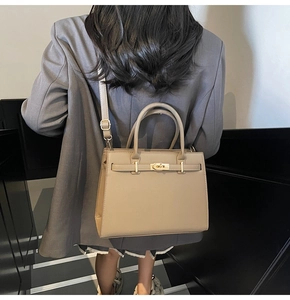 Classic beige Kelly style handbag with gold lock shown on model in grey suit