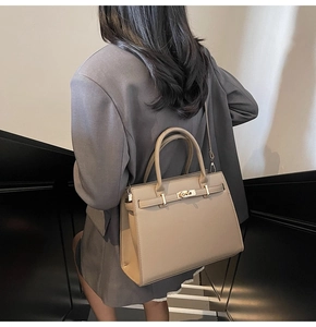 Detailed view of khaki leather handbag with metal turn-lock on a model in a modern setting