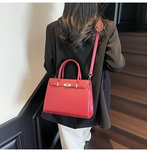 Detail of red pebbled leather handbag with gold metal lock on a model in a suit