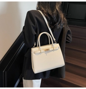 Close-up of cream leather bag featuring golden twist lock and reinforced top handle details