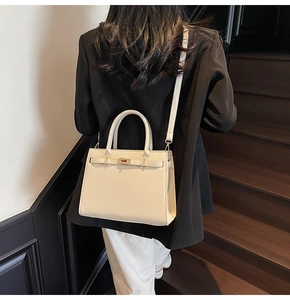 Detail of a cream structured Kelly-style handbag with metal twist lock and shoulder strap