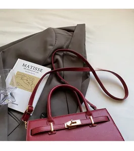 Detail of burgundy lychee grain leather Kelly bag with gold metal rotary lock and strap