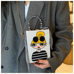 Detail view of white box bag with cartoon girl illustration and striped scarf on handle