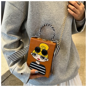 Detail of box clutch bag with cartoon girl pattern, striped scarf handle and gold chain strap