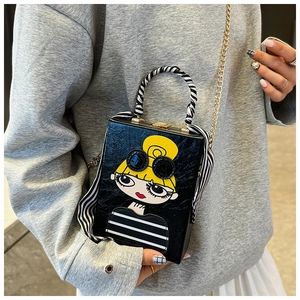 Detail of a black box clutch with fashion girl print, gold chain, and striped scarf handle
