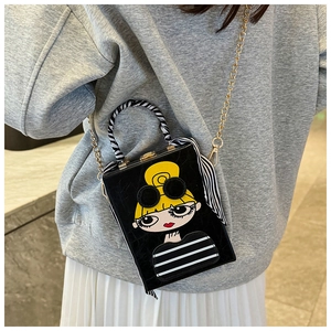 Detail of box clutch bag with cartoon girl print, gold chain, and zebra scarf handle