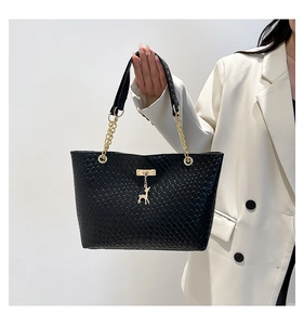 Detail of woven texture tote bag featuring golden chain and deer charm on black leather