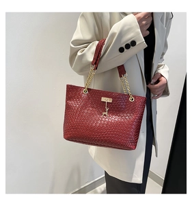 Detail of burgundy woven tote bag with gold chain strap and deer charm on white blazer